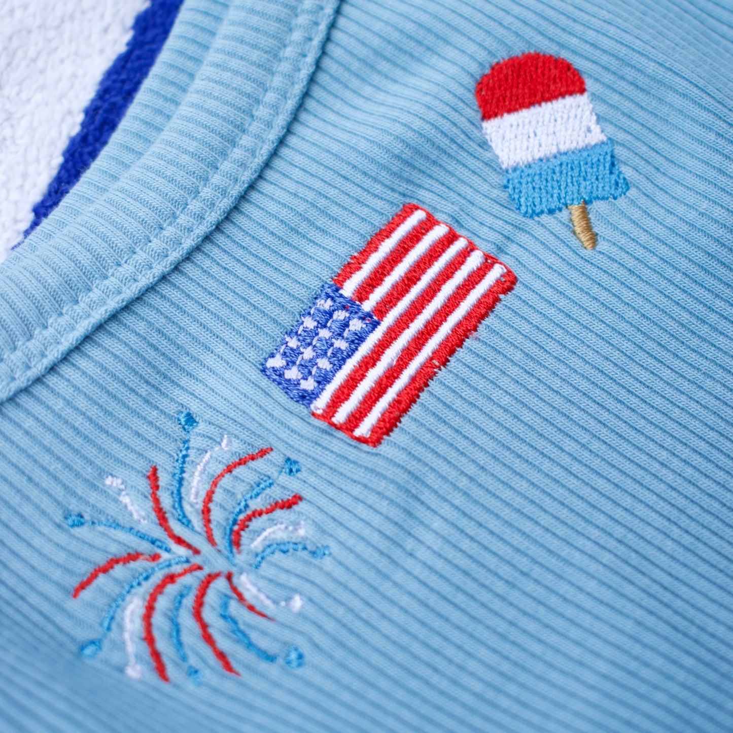 Light blue fabric with embroidered designs of an American flag, a popsicle, and fireworks.