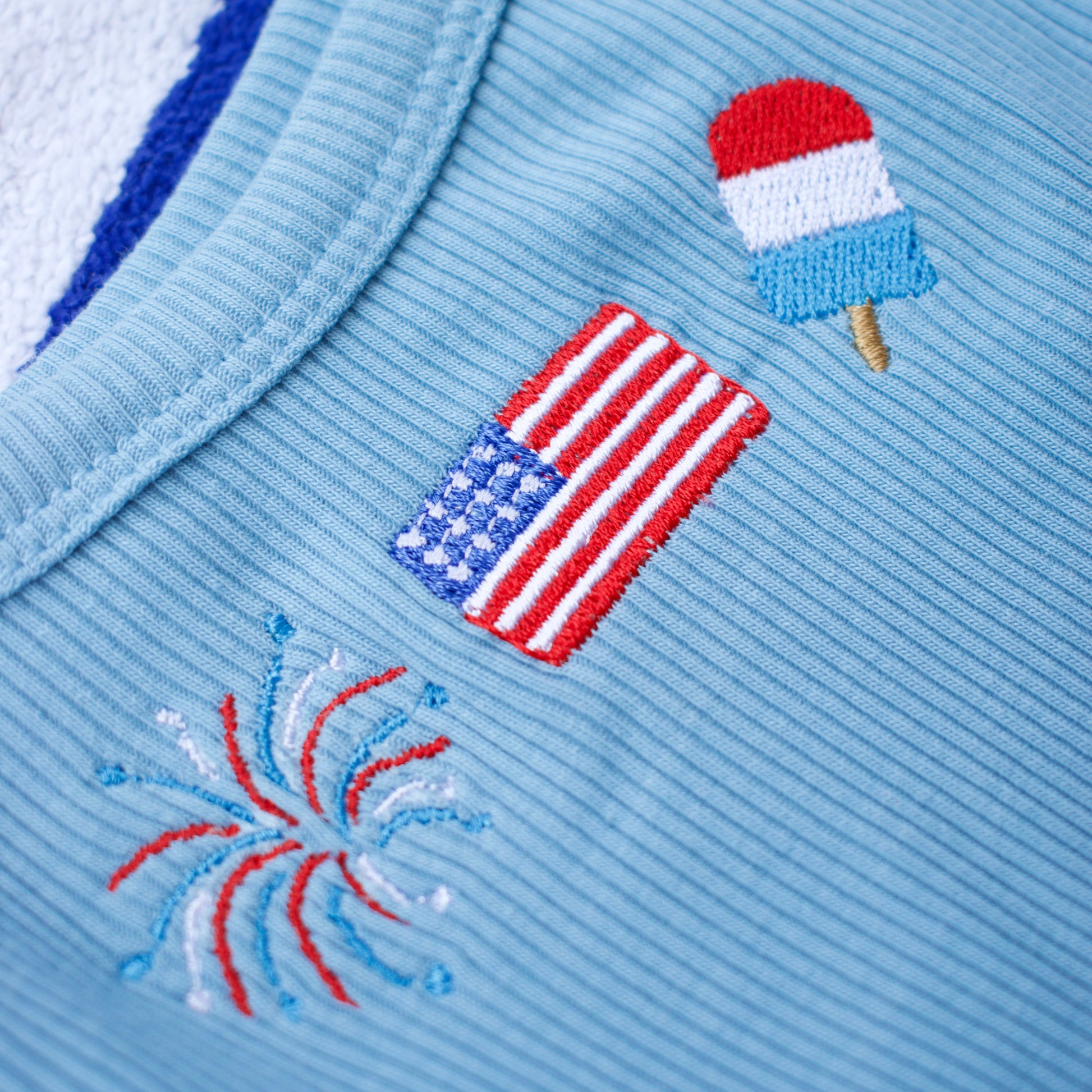 Light blue fabric with embroidered designs of an American flag, a popsicle, and fireworks.